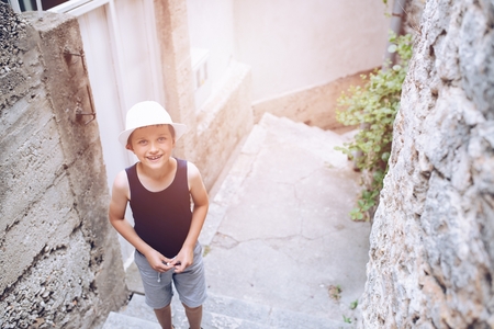 Happy child in white hat walking on narrow street of old town. Child on vacations.の写真素材