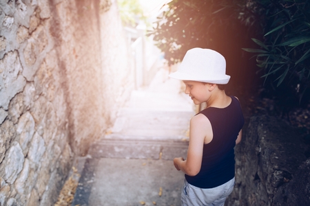 Happy child in white hat walking on narrow street of old town. Child on vacations.の写真素材