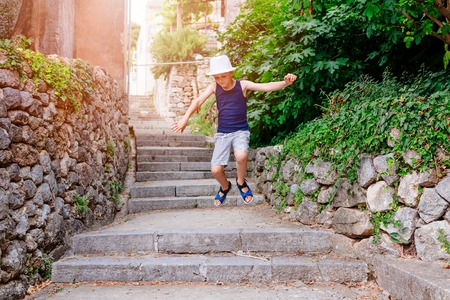 Happy child in white hat walking on narrow street of old town. Child on vacations.の写真素材