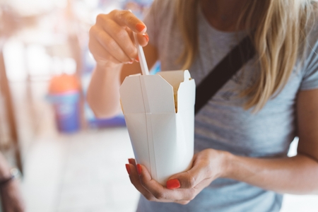 Woman eating fast food noodles from white carton boxの写真素材