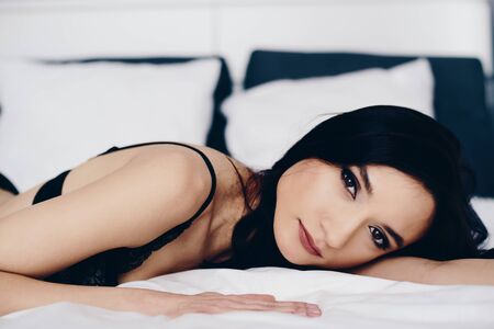 Beautiful young brunette woman relaxing and resting in bed at the morningの写真素材