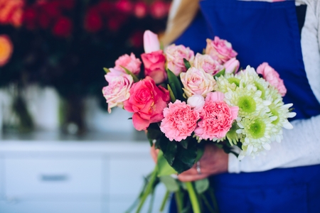 Young woman owner of florist shop making a composition of pink roses. Wearing blue apron. Small business conceptの写真素材