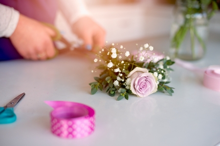 Woman owner of florist shop preparing bouquet of pink roses. Wearing blue apron. Small business conceptの写真素材