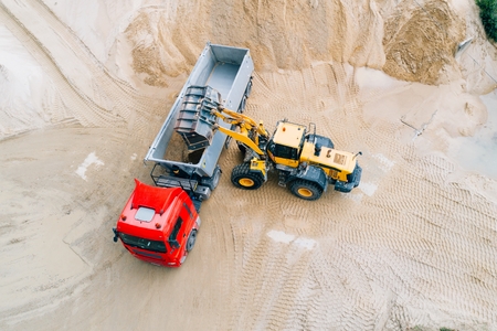 Yellow wheel loader loading sand on dumper truck. Sand quarryの写真素材