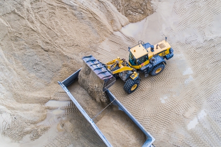 Yellow wheel loader loading sand on dumper truck. Sand quarryの写真素材