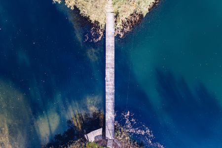 Aerial drone view on two little islands on the lake connected by small wooden bridge. Autumn at the lakeの写真素材