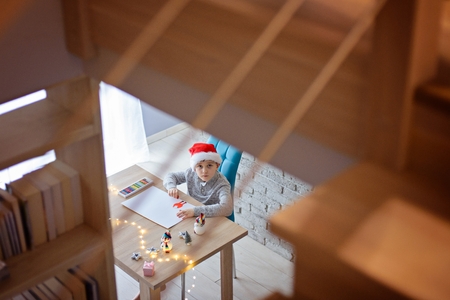 Child in Santa Claus cap drawing a pastel drawing for Santa Claus or writing a wish list.の写真素材