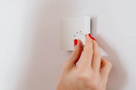 Woman regulating temperature on home heating thermostat on the wallの写真素材