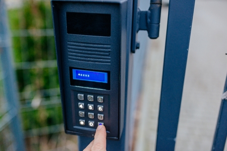 Man opening automatic property gate with security code on outdoor intercom