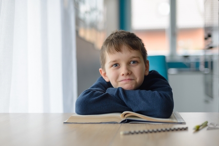 Happy 8 years old boy doing his homework at the table. Child reading a bookの写真素材
