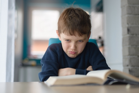 Tired 8 years old boy doing his homework at the table. Child reading a book at the desk.の写真素材