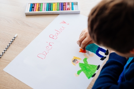 Happy Polish child drawing a greeting card for his grandma. Polish word Grandmother Day!の写真素材
