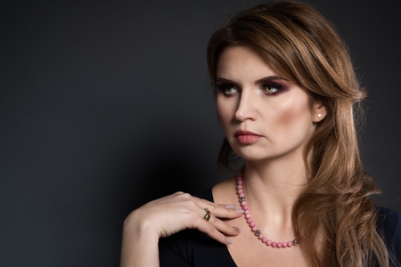 Studio beauty shot of woman with pink pearl necklace. Beautiful young woman posing with jewelry. Dark backgroundの写真素材