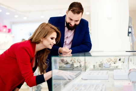 Young couple choosing wedding rings in jewelry store. Woman showing jewelry in the showcase of the jewelry storeの写真素材