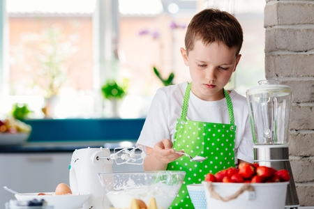 Happy child boy adding sugar to bowl and preparing a cake. Child helping in kitchenの写真素材