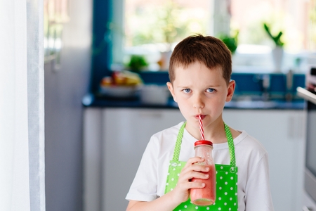 Child boy drinking strawberry smoothie from glass with strawの写真素材