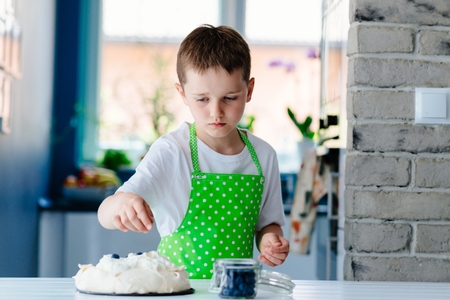 Happy child decorating meringue with blueberries . Child helping in kitchenの写真素材