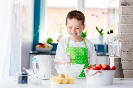 Happy child boy trying sweet dough and preparing a cake. Child helping in kitchenの写真素材