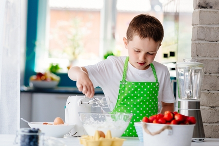 Happy child boy mixing dough in glass bowl and preparing a cake. Child helping in kitchenの写真素材