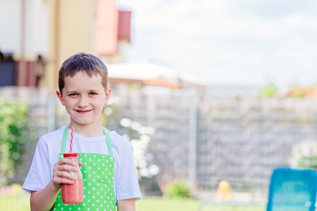 Child boy drinking strawberry smoothie from glass with strawの写真素材