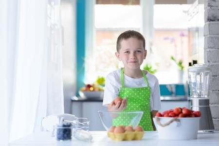 Child boy holding egg. Child helping in kitchenの写真素材