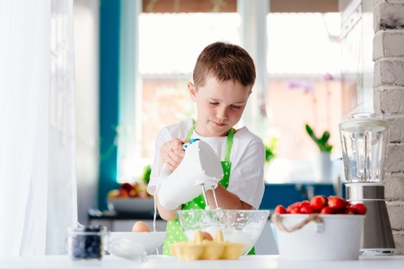 Happy child boy mixing in glass bowl and preparing a cake. Child helping in kitchenの写真素材