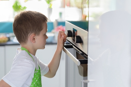 Child boy regulating temperature of the oven. Child helping in kitchenの写真素材