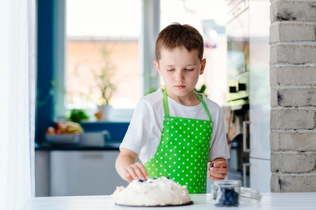 Happy child decorating meringue with blueberries . Child helping in kitchenの写真素材