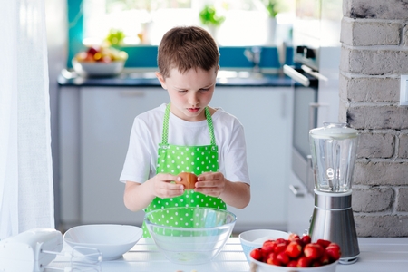 Child boy cracking egg and separating the yolk. Child helping in kitchen. Boy baking cakeの写真素材
