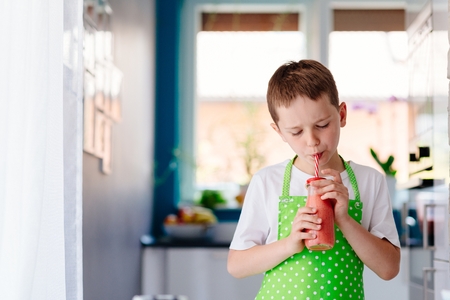 Child boy drinking strawberry smoothie from glass with strawの写真素材