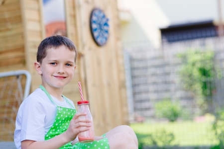 Child boy drinking strawberry smoothie from glass with strawの写真素材