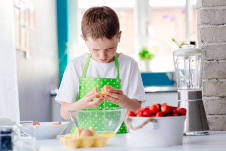Child boy cracking egg and separating the yolk. Child helping in kitchen. Boy baking cakeの写真素材