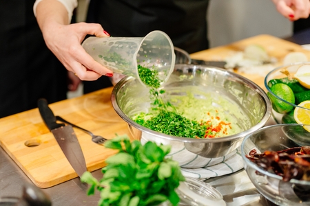 Woman cook adding chopped coriander to the bowl with saladの写真素材
