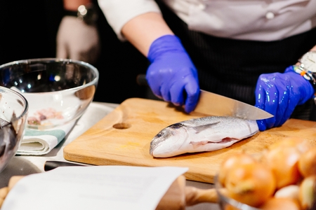 Woman cook preparing and cleaning raw dorada fish with knife on the wooden cutting board in kitchenの写真素材