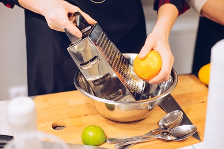 Woman peeling orange on kitchen metal graterの写真素材