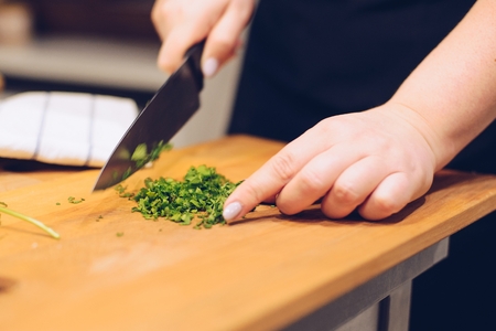 Woman cutting green coriander herb on wooden cutting board in the kitchenの写真素材