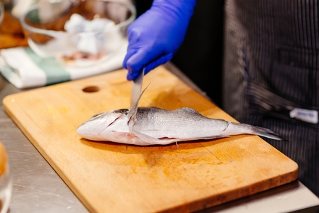 Woman cook preparing and cleaning raw dorada fish with knife on the wooden cutting board in kitchenの写真素材