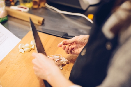 Woman cutting garlic on wooden cutting board in the kitchenの写真素材