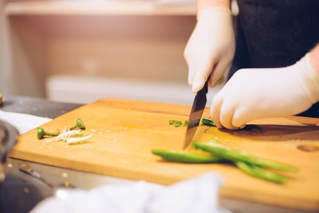 Woman cutting green spicy pepper on wooden cutting board in the kitchenの写真素材