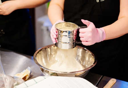 Woman sifting white flour to metal bowl in the kitchenの写真素材