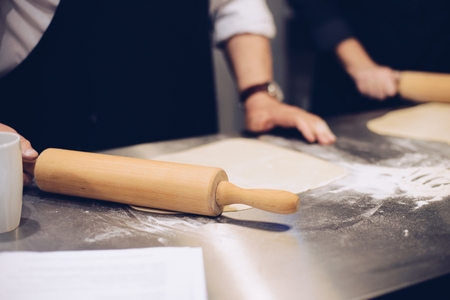 Man rolling raw dough with rolling pin on the tableの写真素材