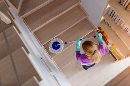 Young woman in white apron cleaning stairs. Cleaning service. Maid cleaning at homeの写真素材