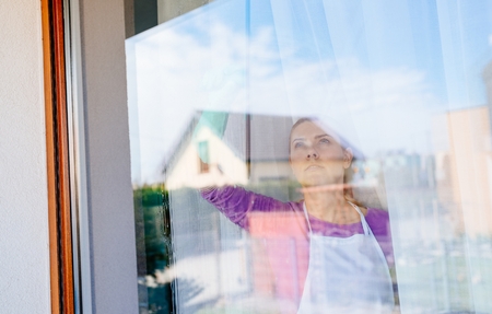 Young beautiful woman in white apron cleaing windows. Cleaning service. Maid cleaning at homeの写真素材