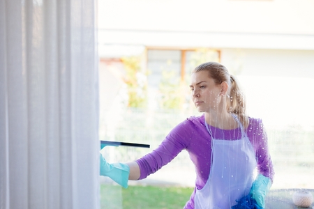 Young woman in white apron washing windows. Cleaning service. Maid cleaning at home