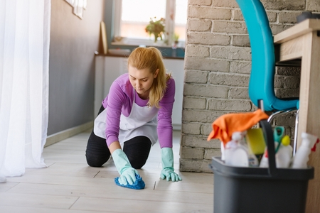 Young beautiful woman in white apron cleaning floor on her knees. Cleaning service. Maid cleaning at homeの写真素材
