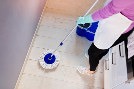 Young beautiful woman in white apron cleaning floor. Cleaning service. Maid cleaning at homeの写真素材