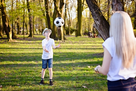 Mother playing with ball with her sons on green grass in park. Happy family in the parkの写真素材