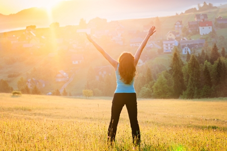 Young happy woman with raised arms in mountains at sunrise. Freedom and relax conceptの写真素材