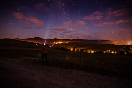 Young happy woman at starry night in mountains. Pointing flashlight light to the sky. Freedom and relax conceptの写真素材
