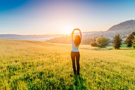 Woman with arms raised up to sky, celebrating new day. Female enjoying life at sunny morning. Happy young woman at mountains. Relaxation and freedom conceptの写真素材